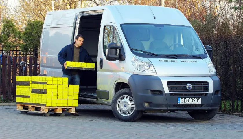 Mężczyzna rozładowuje żółte paczki z Fiata Ducato 2.3.