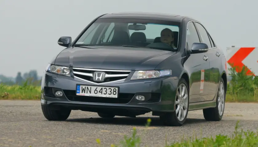 Ciemnoszary Honda Accord z kobietą za kierownicą jedzie po drodze.