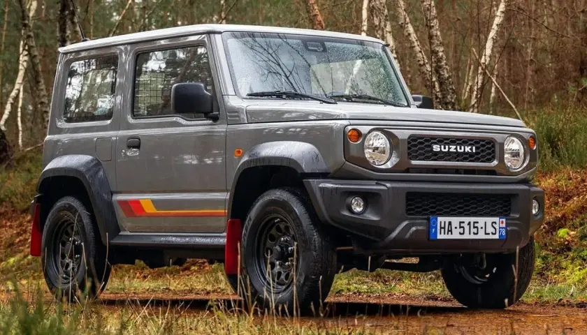 Szary Suzuki Jimny 2026 z kolorowymi pasami na boku, gotowy na terenową przygodę w lesie.