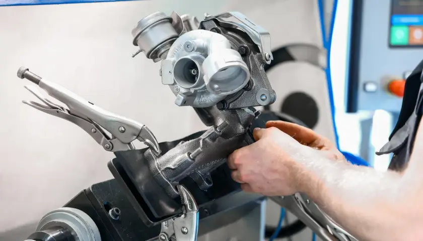 Mechanik naprawia turbosprężarkę, mocując ją imadłem. Widoczny jest zawór N75, kluczowy element sterujący pracą turbiny.