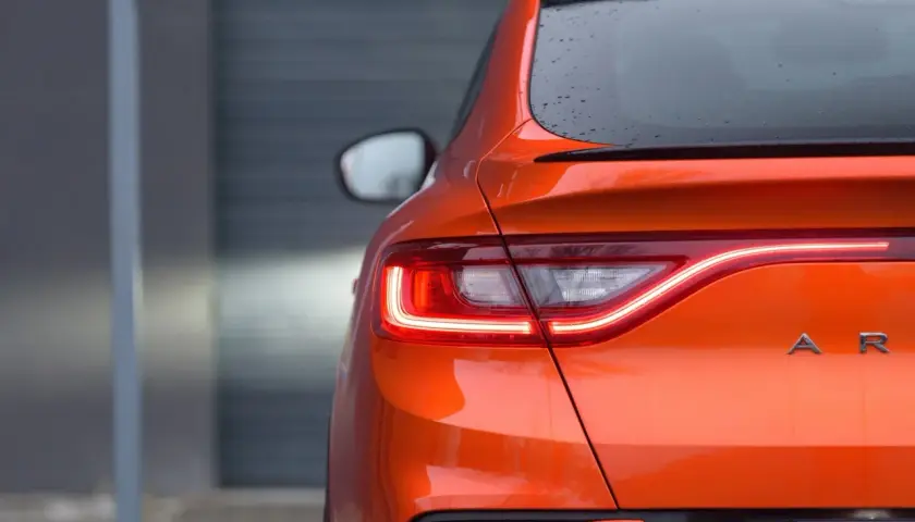 Pomarańczowy Renault Arkana z włączonymi światłami LED. Zbliżenie na tylną część auta, gdzie widoczne są detale nadwozia i nazwa modelu. Idealne wymiary dla miejskiej dżungli.