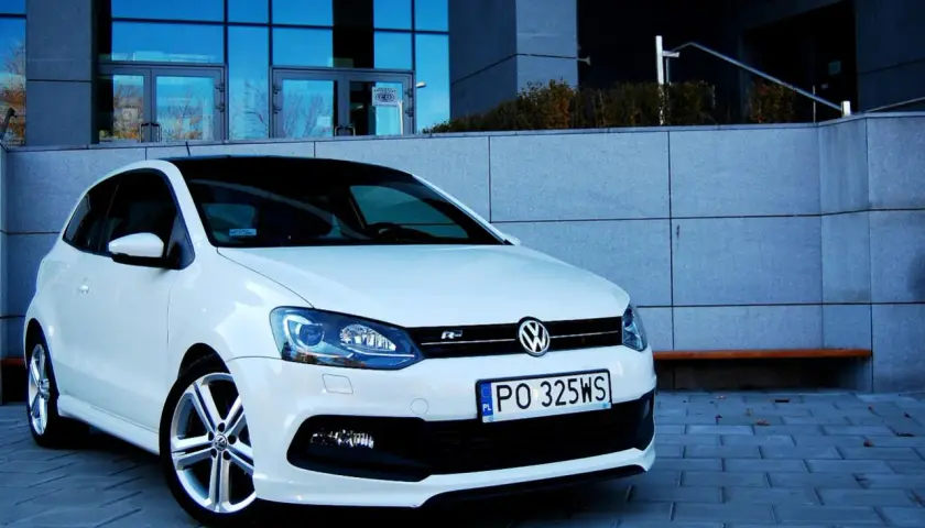 Biały VW Polo 1.2 benzyna z czarnym dachem, zaparkowany przed nowoczesnym budynkiem.