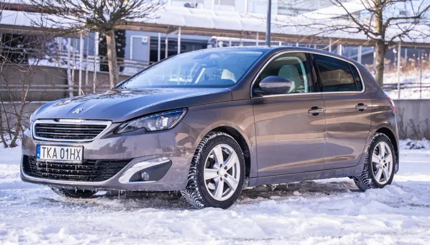 Szary Peugeot 308 na zimowych oponach, gotowy na śnieżne drogi. Wiele pozytywnych peugeot 308 opinie potwierdza jego wszechstronność.
