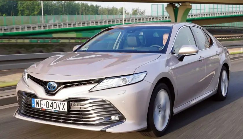 Elegancka, beżowa Toyota Camry 2023 na drodze, z kierowcą za kierownicą.
