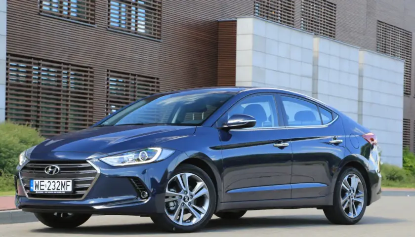 Ciemnoniebieski Hyundai Elantra 2023 zaparkowany przed nowoczesnym budynkiem z drewnianą fasadą.
