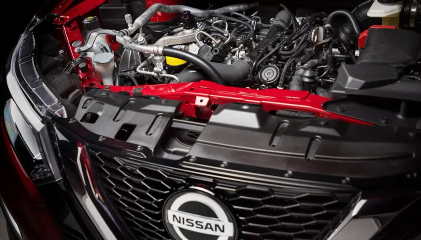 Silnik 1.6 benzyna w Nissan Qashqai. Czerwone elementy karoserii i skomplikowana sieć przewodów pod maską.