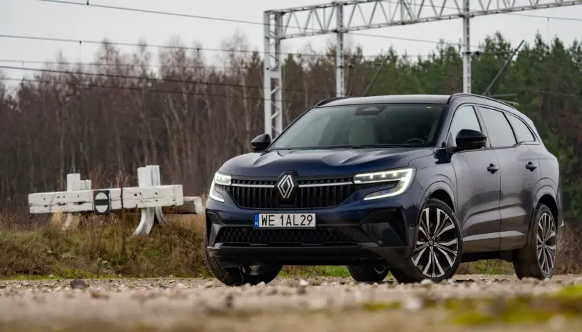 Nowy Renault Espace 2024, ciemnoniebieski SUV, zaparkowany przy torach kolejowych, gotowy na przygodę.