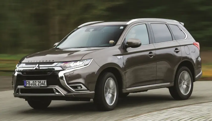 Brązowy Mitsubishi Outlander PHEV jedzie po drodze, z rozmytym tłem lasu.
