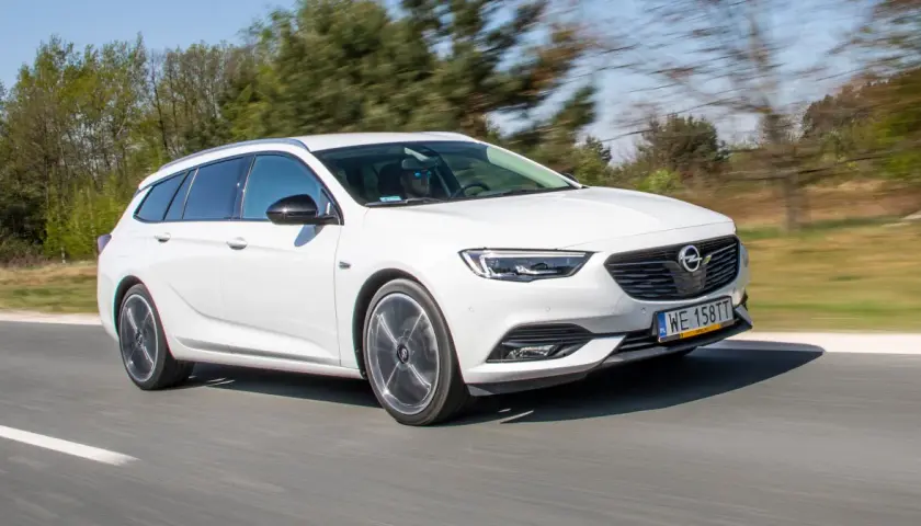 Białe kombi Opel Insignia 2.0 CDTI pędzi po drodze, za kierownicą mężczyzna w okularach przeciwsłonecznych.