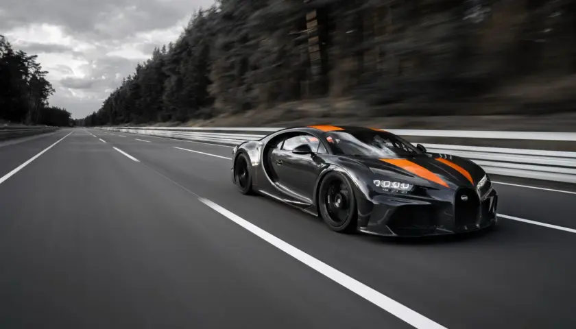 Czarny Bugatti Chiron Super Sport z pomarańczowymi pasami pędzi po pustej autostradzie.
