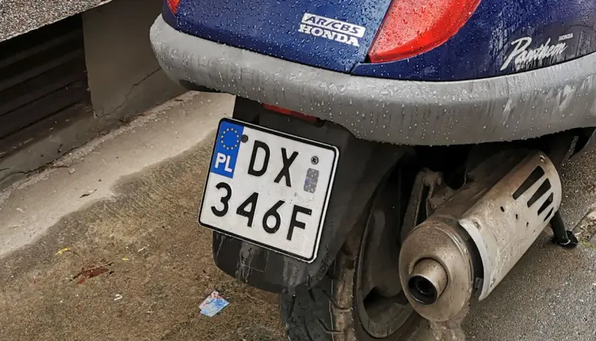 Skuter Honda Pantheon z tablicą rejestracyjną DX 346F, gotowy do jazdy po deszczu.