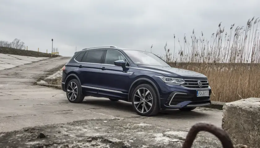 Ciemnoniebieski Volkswagen Tiguan Allspace na betonowej drodze, w tle trzciny i pochmurne niebo.