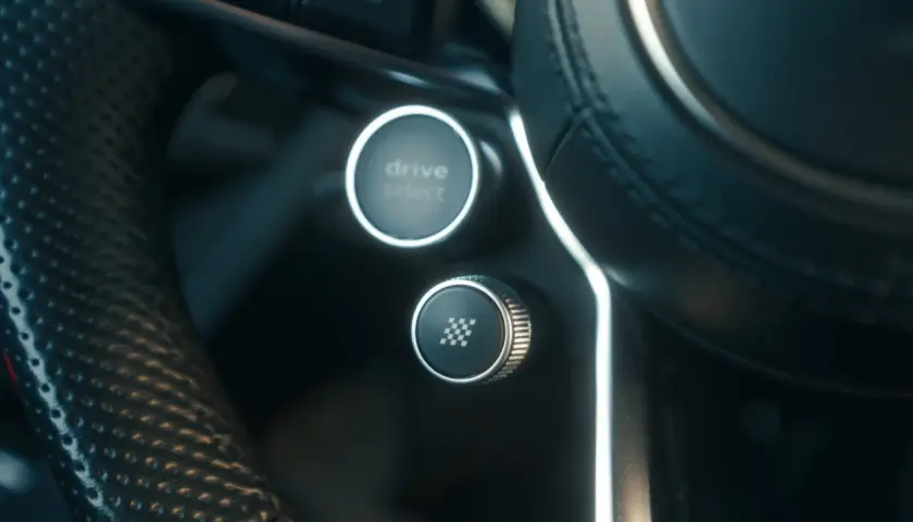 Przycisk z szachownicą na kierownicy, gotowy do aktywacji launch control. Obok przycisk Drive Select.