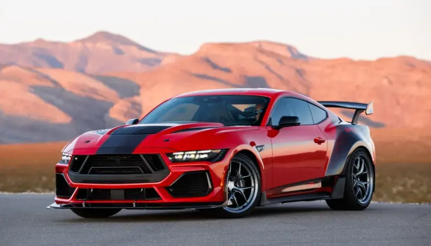 Czerwony mustang shelby z czarnymi pasami i spojlerem na tle pustynnych gór.