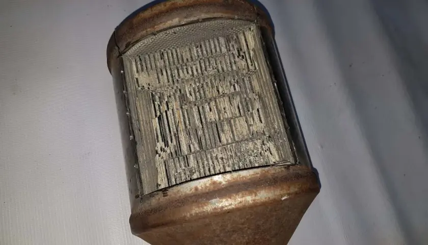 Zardzewiały, uszkodzony katalizator samochodowy, przypominający strukturą plaster miodu. FAP w złym stanie.