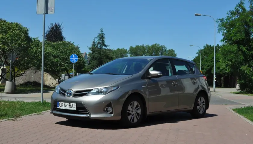 Szary Toyota Auris na tle zieleni i błękitnego nieba. Wiele osób szuka toyota auris opinie przed zakupem.