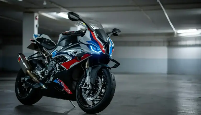 Sportowy motocykl BMW XR w biało-niebiesko-czerwonych barwach, z włączonymi światłami LED, stoi na betonowej posadzce w garażu.