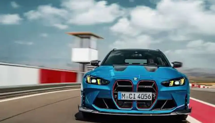 Niebieskie BMW M3 Competition pędzi po torze wyścigowym, chmury na niebie dodają dynamiki.