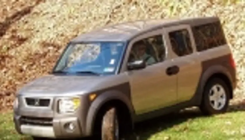Srebrny Honda Element z brązowymi akcentami stoi na trawie, na tle zbocza pokrytego liśćmi.