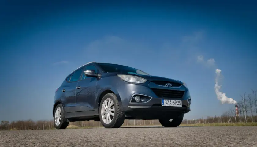 Szary Hyundai ix35 na tle błękitnego nieba. W tle komin z dymem. Wiele pozytywnych hyundai ix35 opinie potwierdza jego wszechstronność.