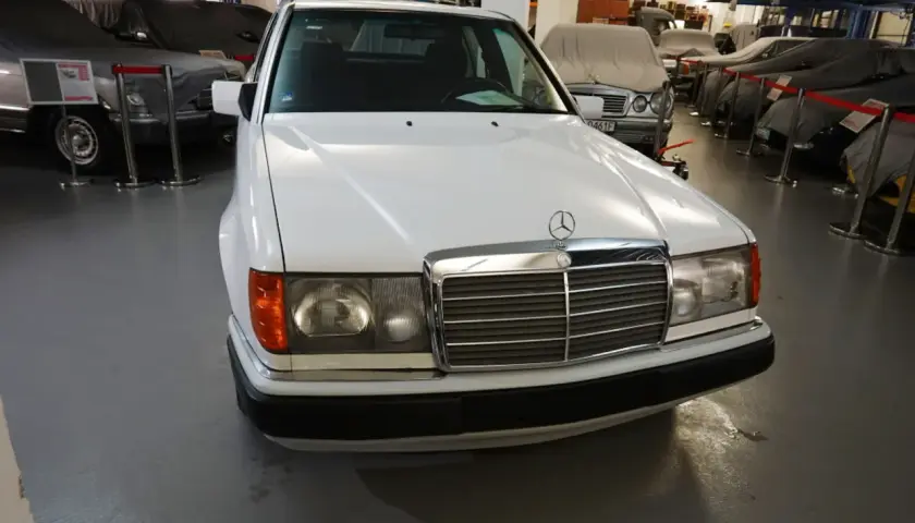 Biały Mercedes "Baleron" z lat 80. stoi w muzeum obok innych zakrytych samochodów.