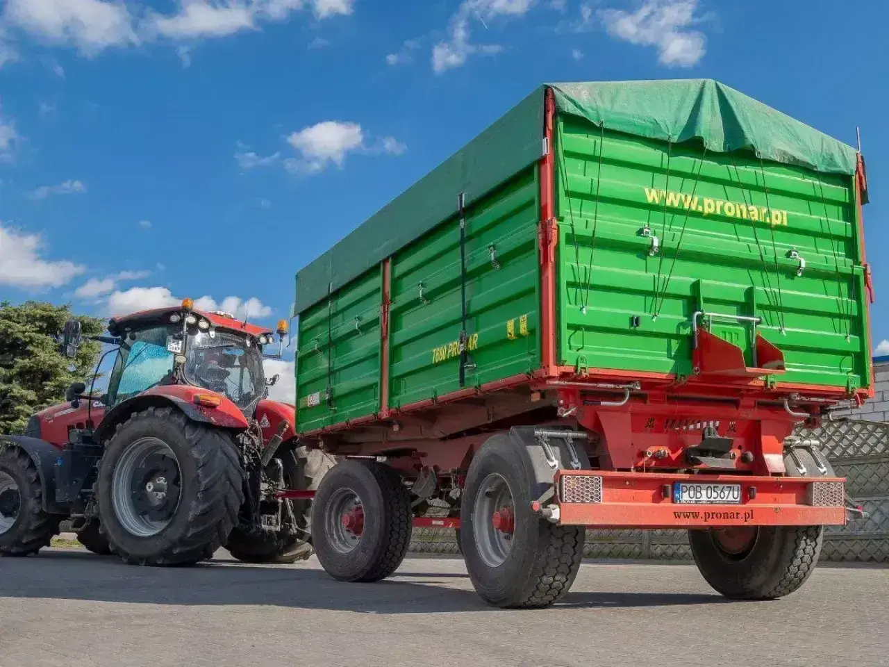 Czerwony traktor z zieloną przyczepą. Zastanawiasz się, ile można jechać z przyczepką? Ten zestaw jest gotowy do pracy.