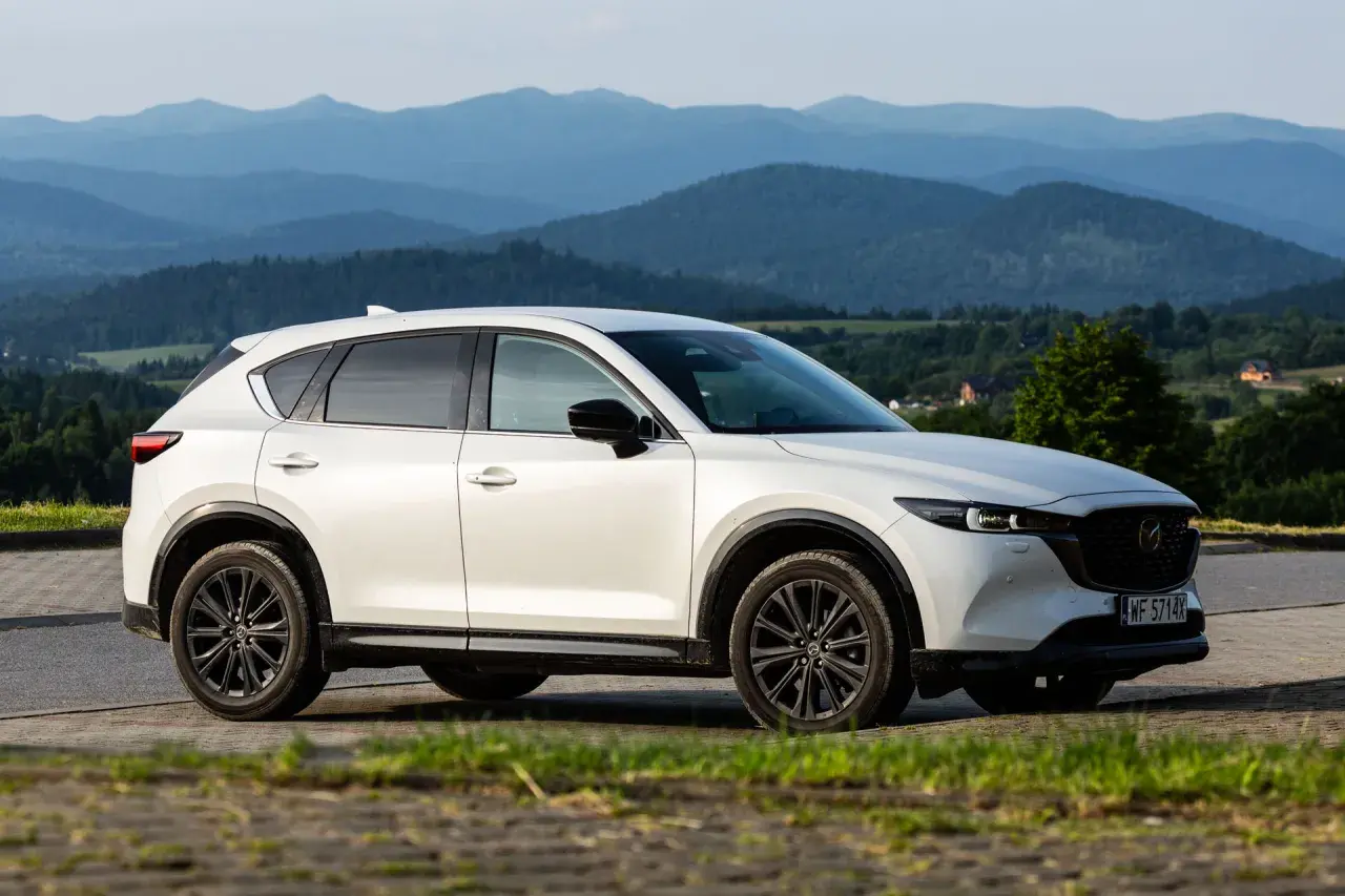 Biała Mazda CX-5 z czarnymi felgami na tle górskiego krajobrazu. KSU rejestracja widoczna na tablicy.