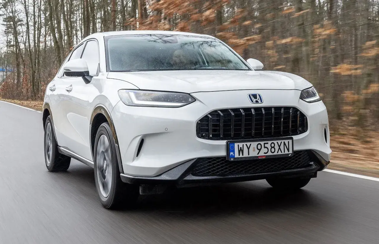 Biała Honda ZR-V przemierza leśną drogę, ukazując swój elegancki design i dynamiczną sylwetkę.