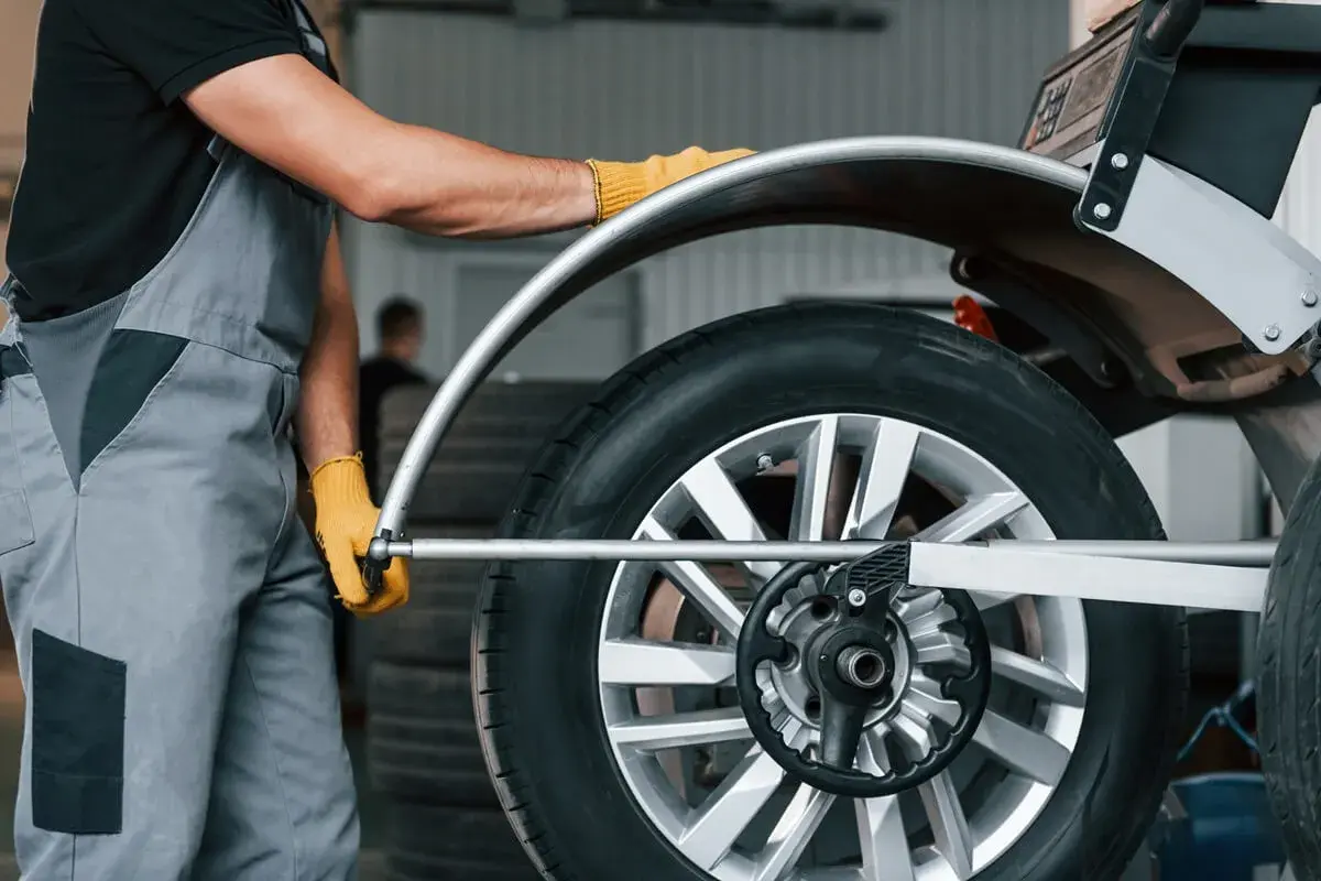 Mechanik w żółtych rękawiczkach ustawia koło na wyważarce. Dowiedz się, ile kosztuje wyważenie kół.