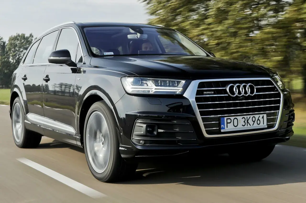 Czarny Audi Q7 3.0 TDI pędzi po drodze, otoczony zielenią drzew.