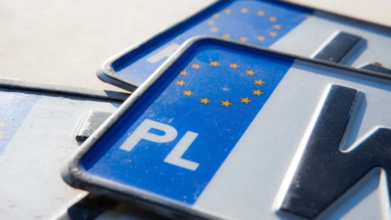 Zbliżenie na polskie tablice rejestracyjne z symbolem Unii Europejskiej. Widoczne litery "PL" i fragmenty numerów.