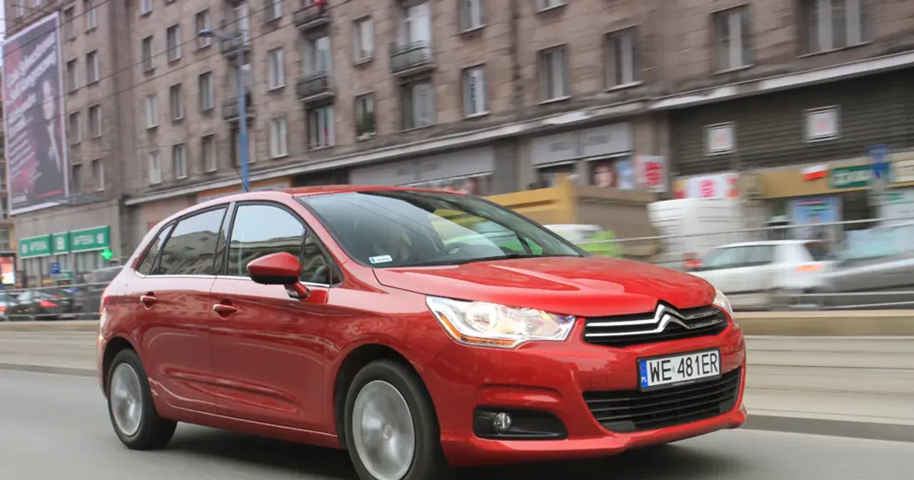 Czerwony Citroen C4 1.6 HDi w ruchu miejskim, z rozmytym tłem budynków i innych pojazdów.
