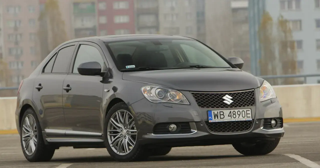 Szary Suzuki Kizashi z polskimi tablicami WB 4890E zaparkowany na tle bloków mieszkalnych.