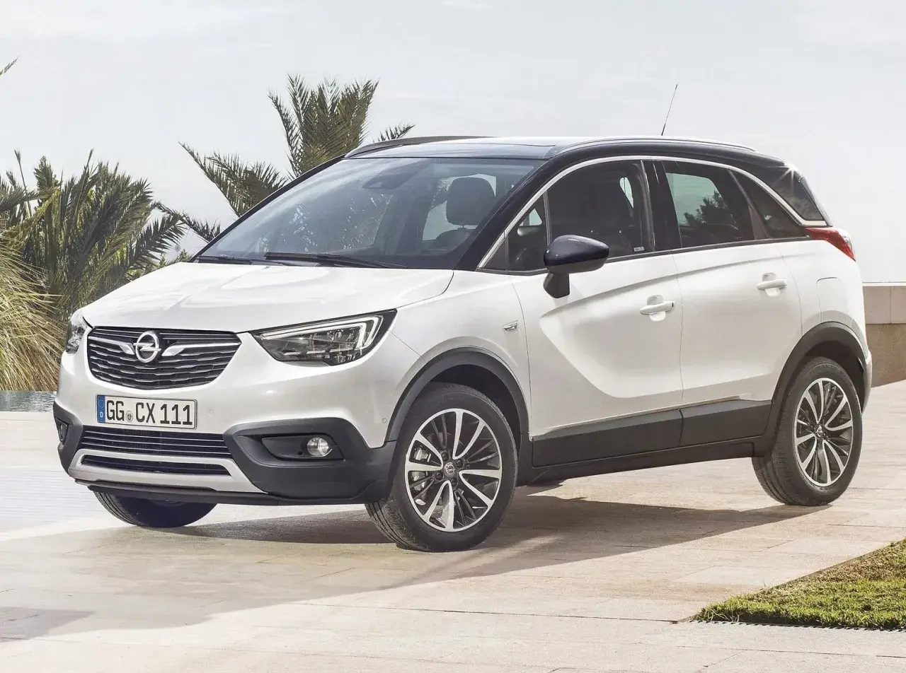 Biały Opel Crossland z czarnym dachem, zaparkowany na tarasie przy basenie. Wiele osób szuka opinii o tym modelu.