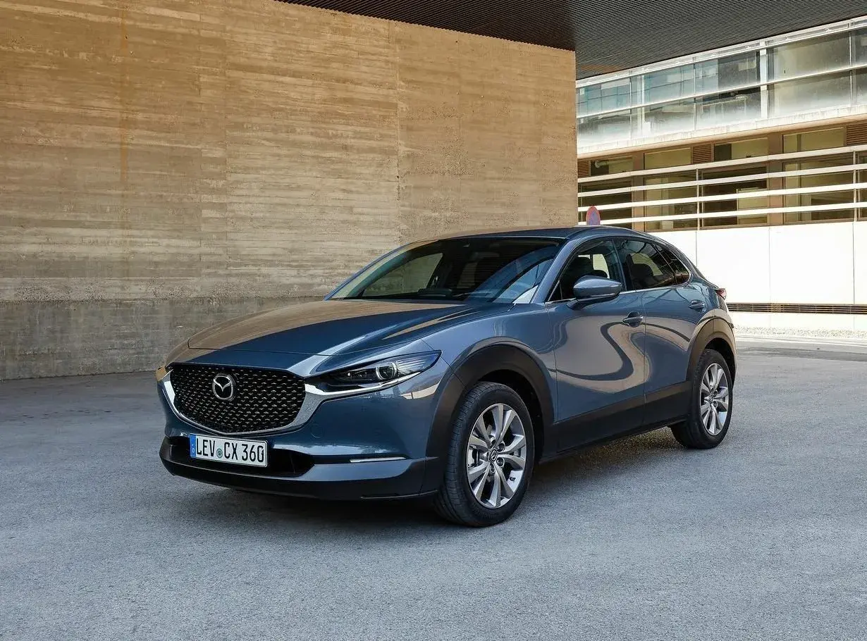 Szary Mazda CX-30 stoi przed betonową ścianą. Wady tego modelu to m.in. ograniczona widoczność z tyłu.