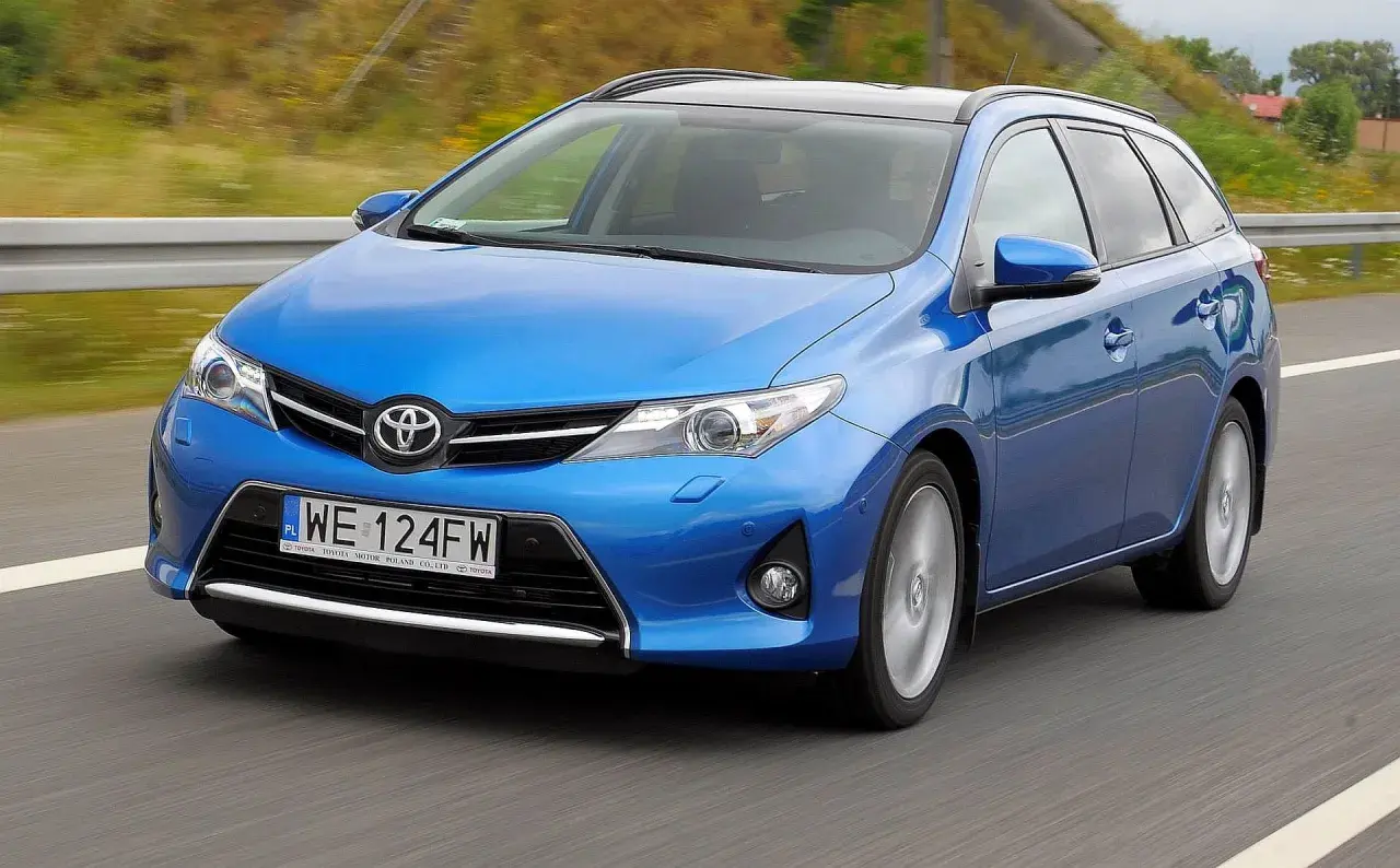 Niebieski Toyota Auris 1.6 benzyna w wersji kombi jedzie po drodze.