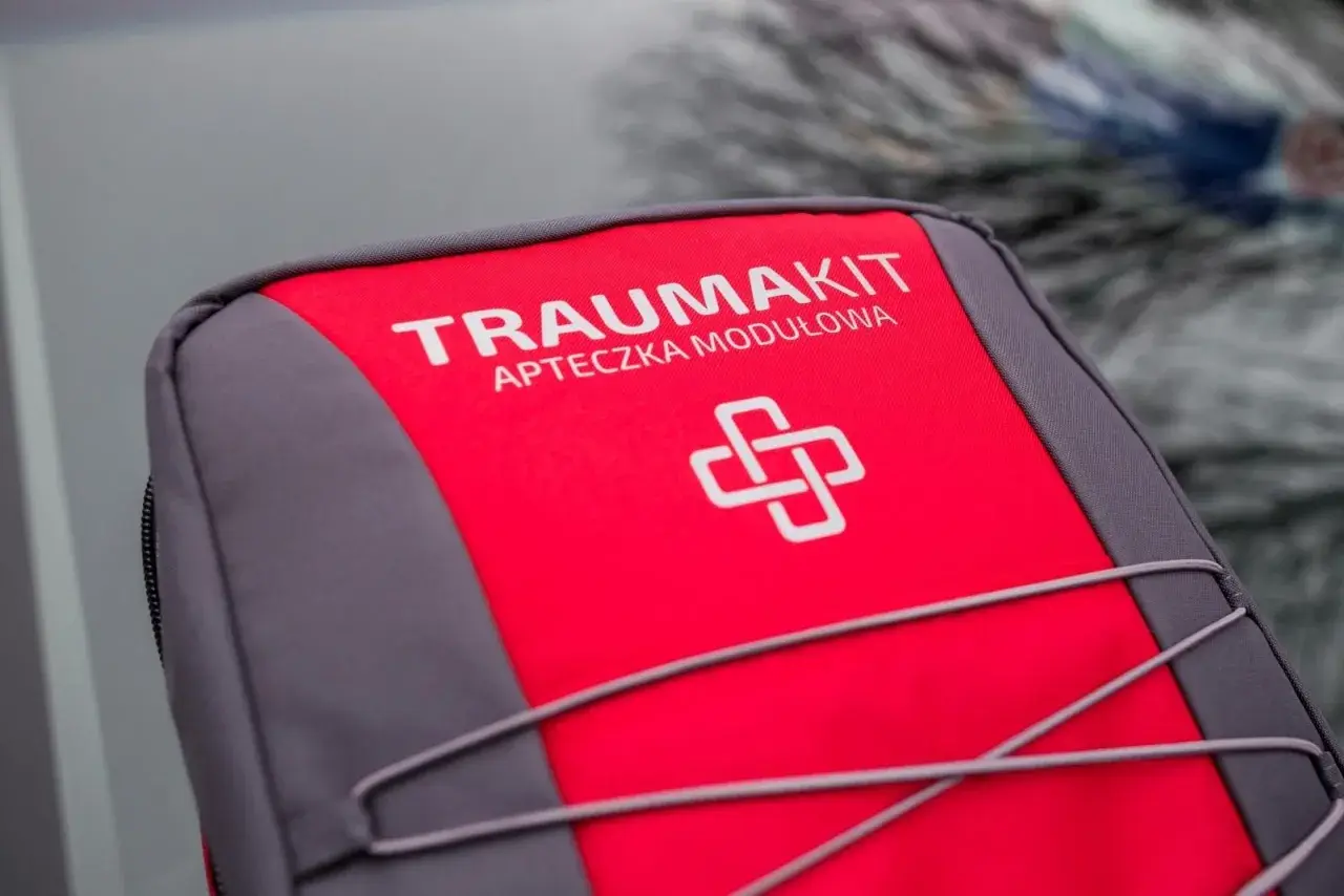 Czerwono-szara apteczka "Trauma Kit" z symbolem krzyża. Czy apteczka jest obowiązkowa w samochodzie? Zawsze warto ją mieć!