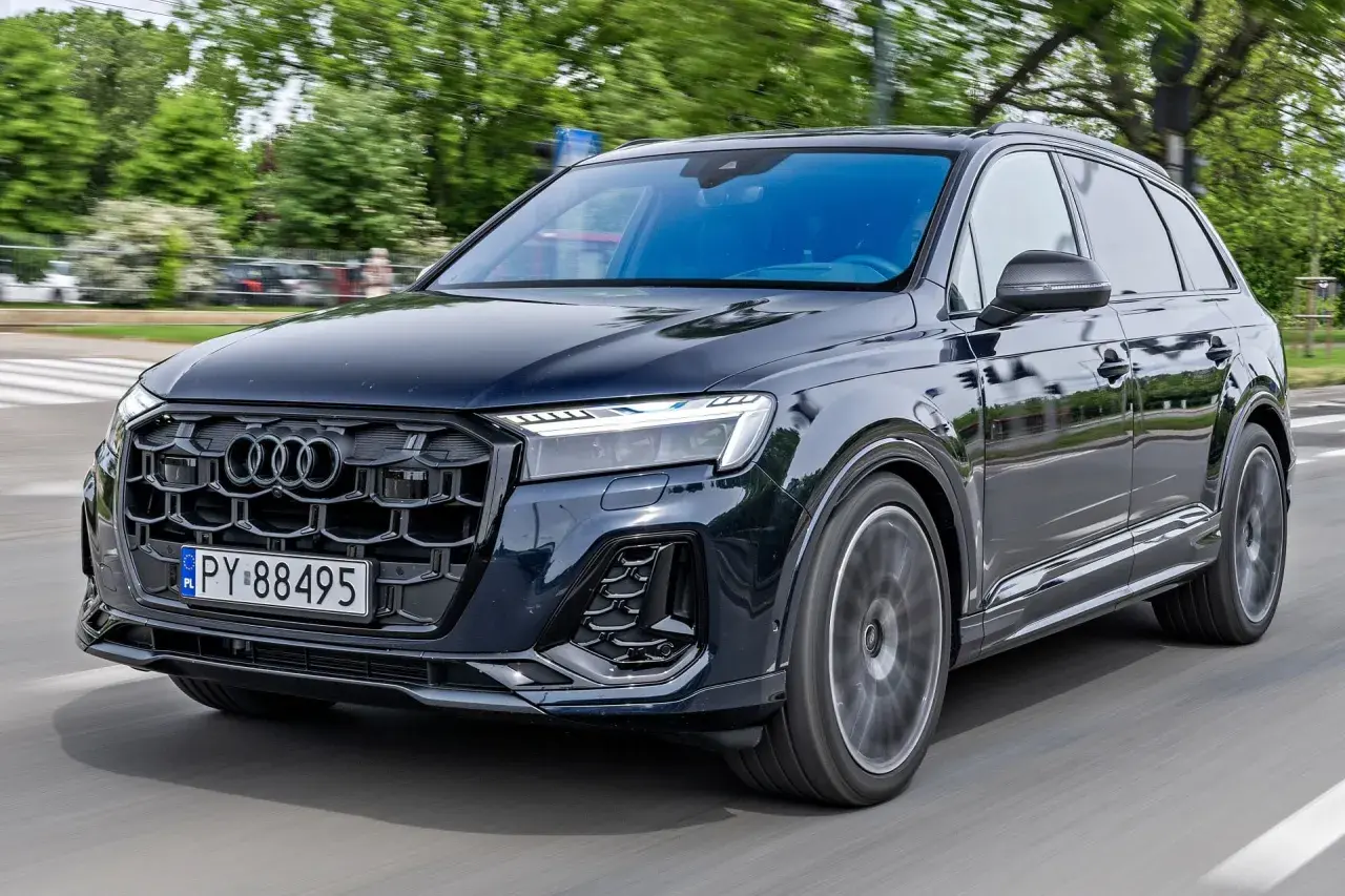 Ciemny Audi Q7 w ruchu ulicznym. Zbliżenie na przednią część pojazdu, widoczna atrapa chłodnicy i reflektory. Poznaj audi q7 wymiary.