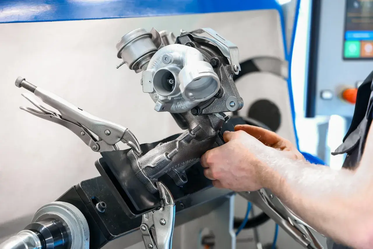 Mechanik naprawia turbosprężarkę, mocując ją imadłem. Widoczny jest zawór N75, kluczowy element sterujący pracą turbiny.