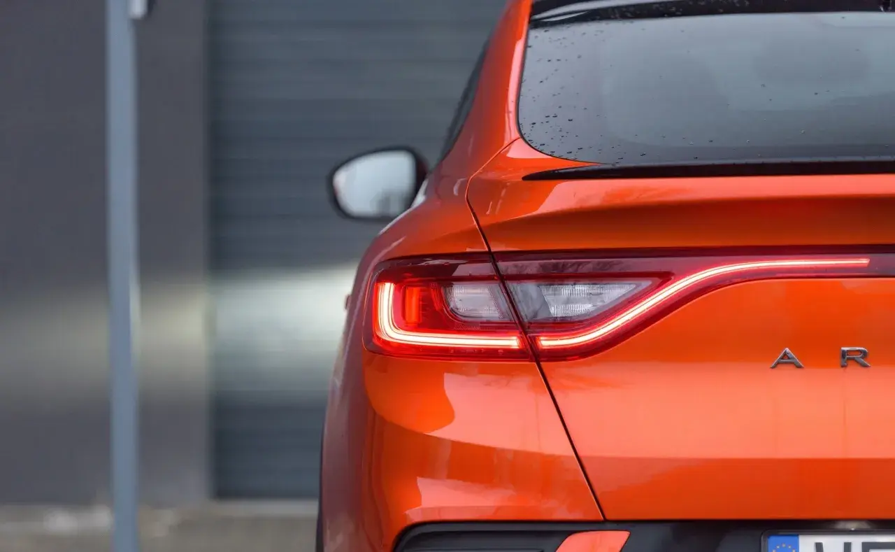 Pomarańczowy Renault Arkana z włączonymi światłami LED. Zbliżenie na tylną część auta, gdzie widoczne są detale nadwozia i nazwa modelu. Idealne wymiary dla miejskiej dżungli.