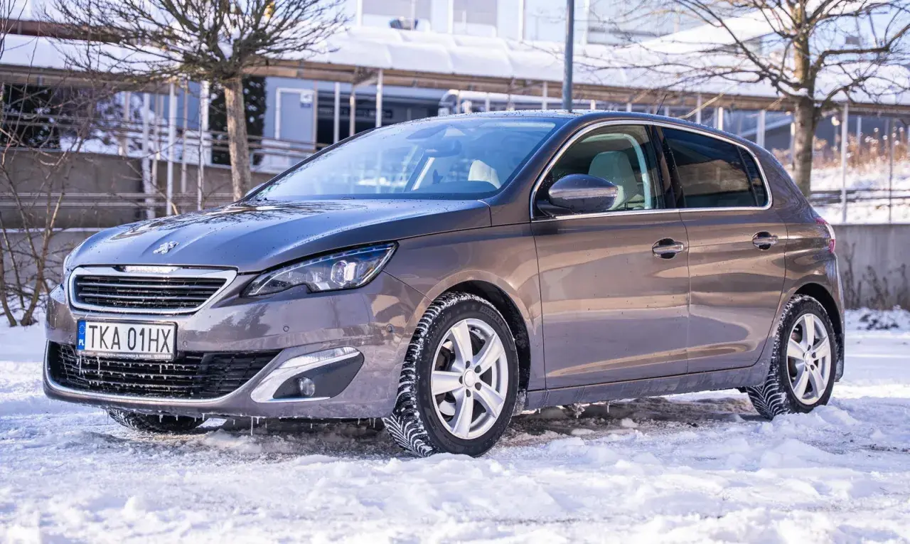 Szary Peugeot 308 na zimowych oponach, gotowy na śnieżne drogi. Wiele pozytywnych peugeot 308 opinie potwierdza jego wszechstronność.