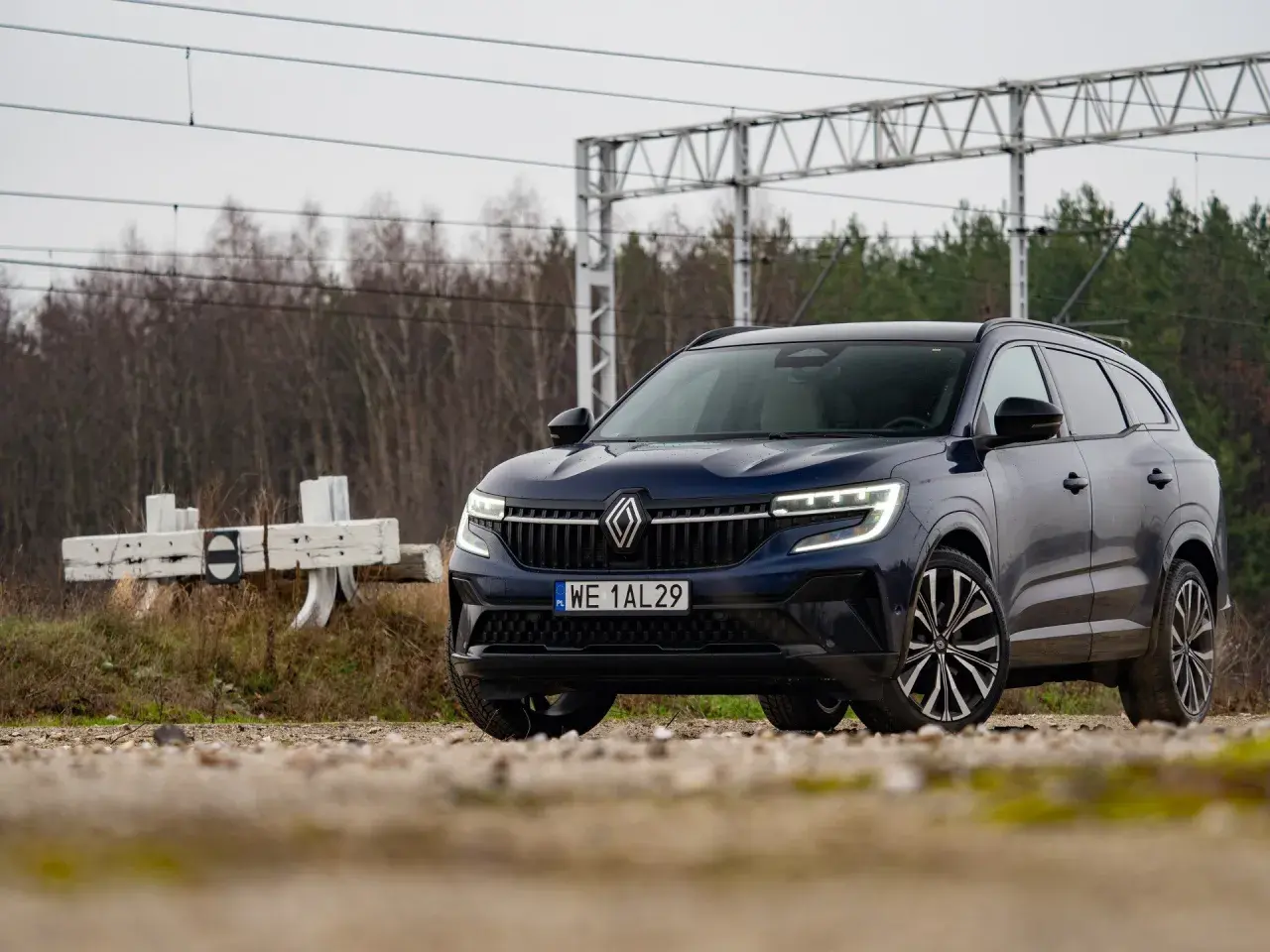 Nowy Renault Espace 2024, ciemnoniebieski SUV, zaparkowany przy torach kolejowych, gotowy na przygodę.