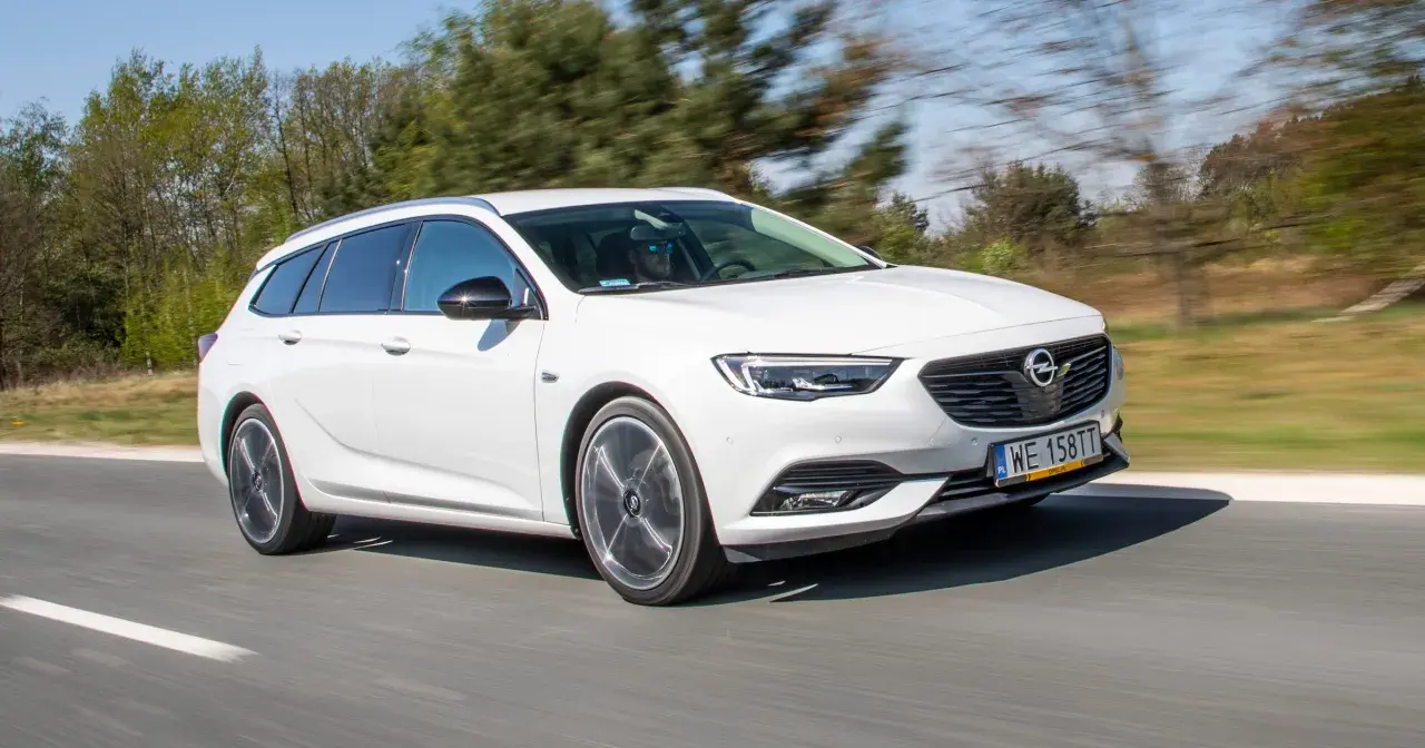 Białe kombi Opel Insignia 2.0 CDTI pędzi po drodze, za kierownicą mężczyzna w okularach przeciwsłonecznych.