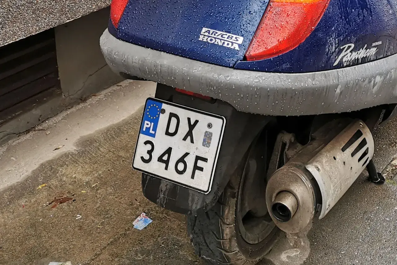 Skuter Honda Pantheon z tablicą rejestracyjną DX 346F, gotowy do jazdy po deszczu.