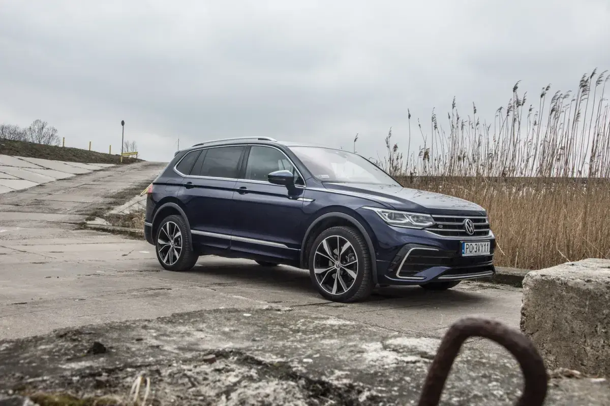 Ciemnoniebieski Volkswagen Tiguan Allspace na betonowej drodze, w tle trzciny i pochmurne niebo.