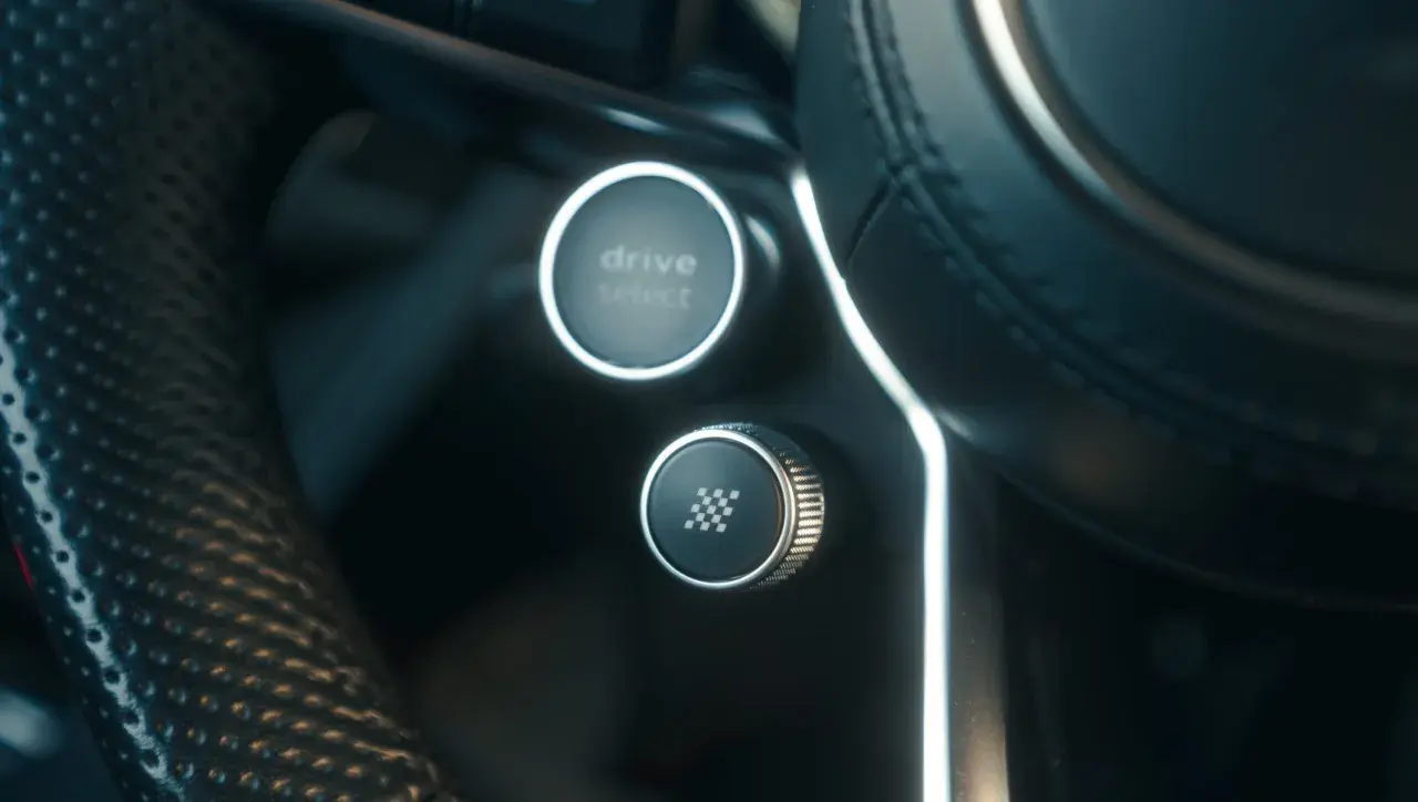 Przycisk z szachownicą na kierownicy, gotowy do aktywacji launch control. Obok przycisk Drive Select.