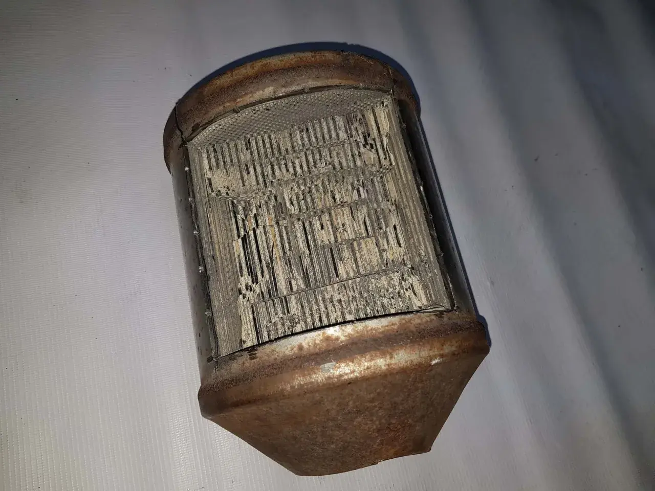 Zardzewiały, uszkodzony katalizator samochodowy, przypominający strukturą plaster miodu. FAP w złym stanie.