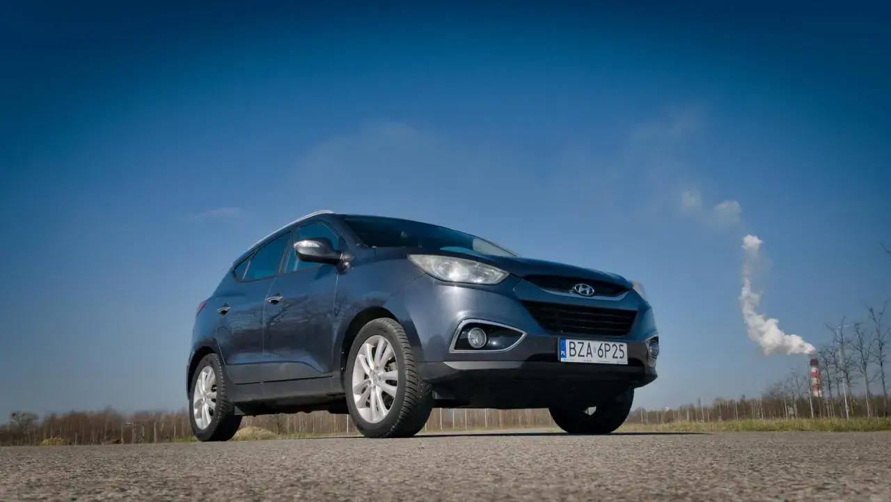 Szary Hyundai ix35 na tle błękitnego nieba. W tle komin z dymem. Wiele pozytywnych hyundai ix35 opinie potwierdza jego wszechstronność.