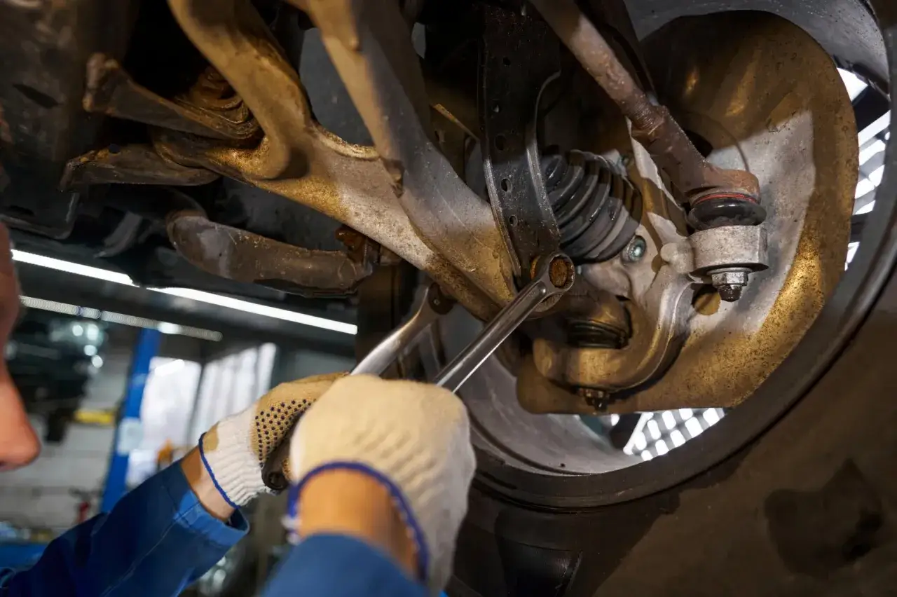 Mechanik w rękawiczkach dokręca śrubę w zawieszeniu samochodu kluczem.