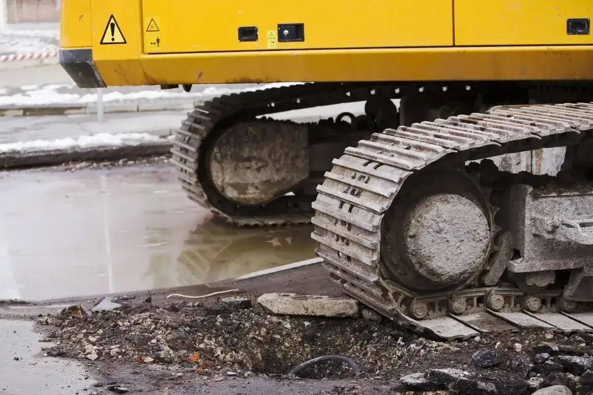 Gąsienice koparki, w tym widoczna zwolnica, pracują na budowie.